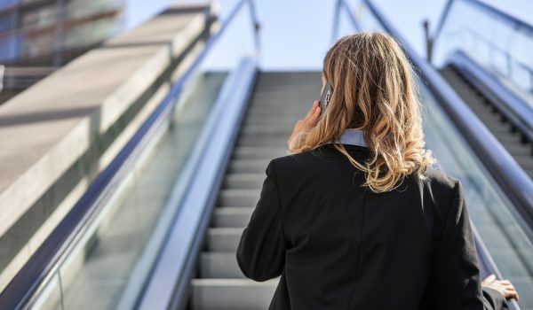 rear-view-businesswoman-suit-standing-escalator-talking-mobile-phone TITLrear-view-businesswoman-suit-standing-escalator-talking-mobile-phone